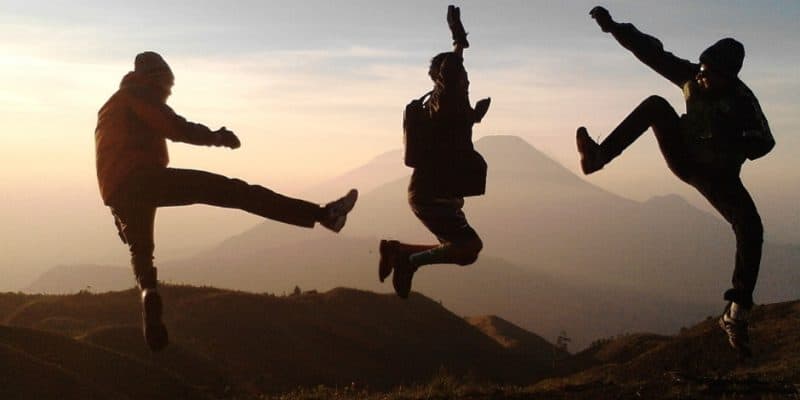 Three people jumping in the air on top of a mountain.
