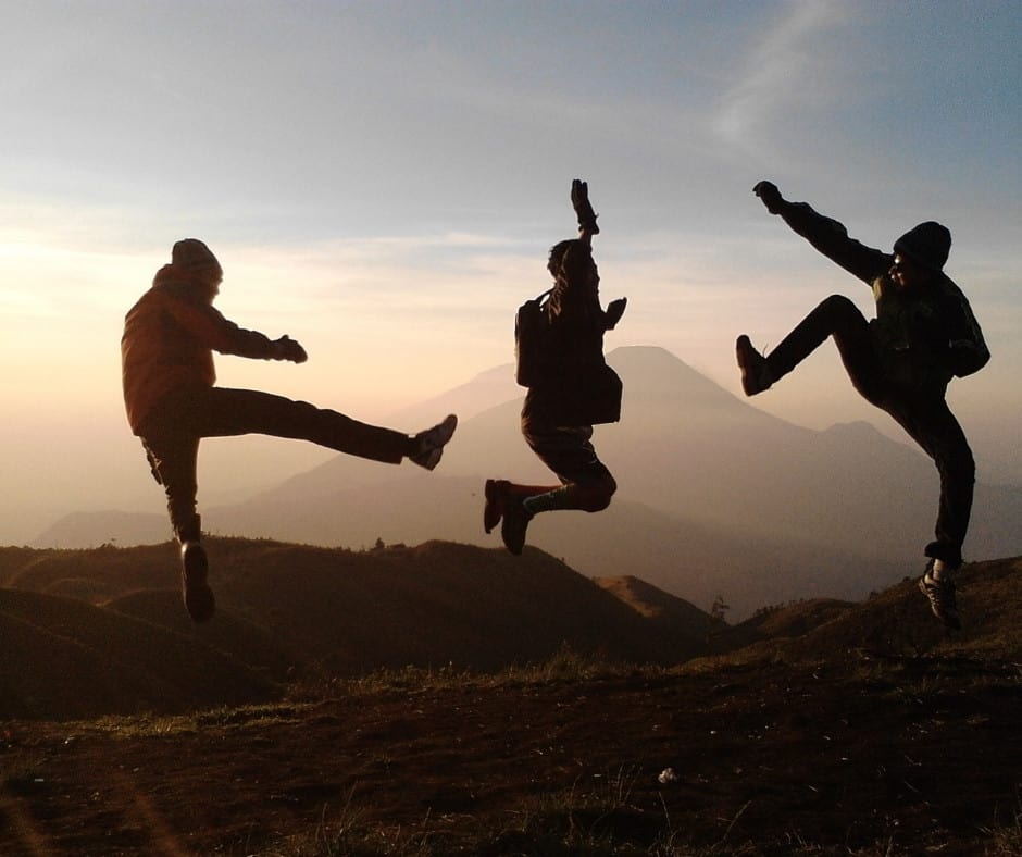 Three people jumping in the air on top of a mountain.