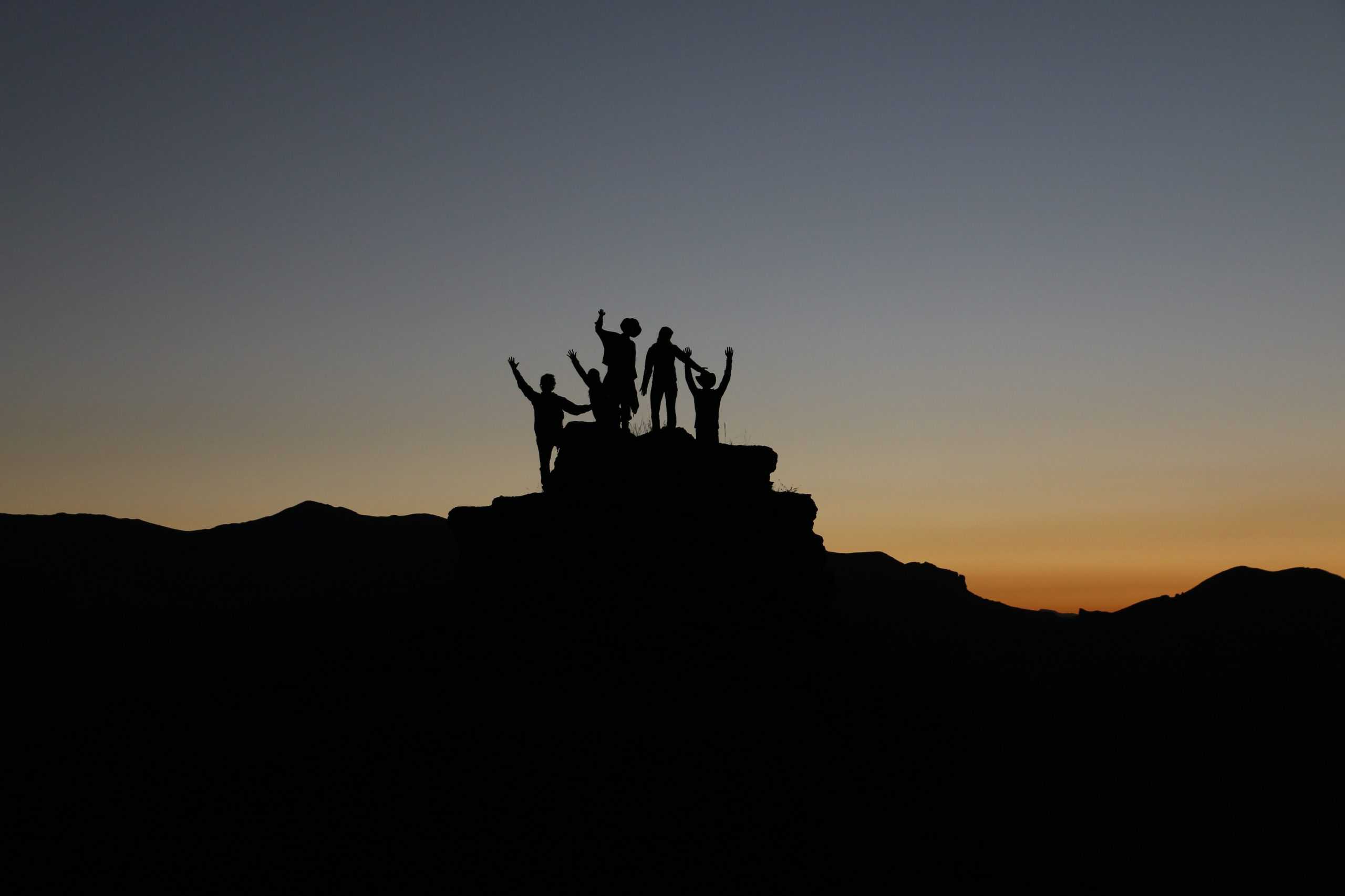 Silhouette of a group of people on top of a mountain.
