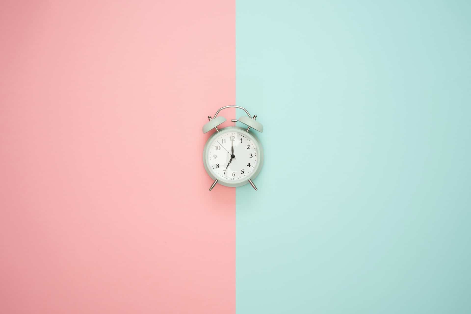 An alarm clock on a pink and blue background.