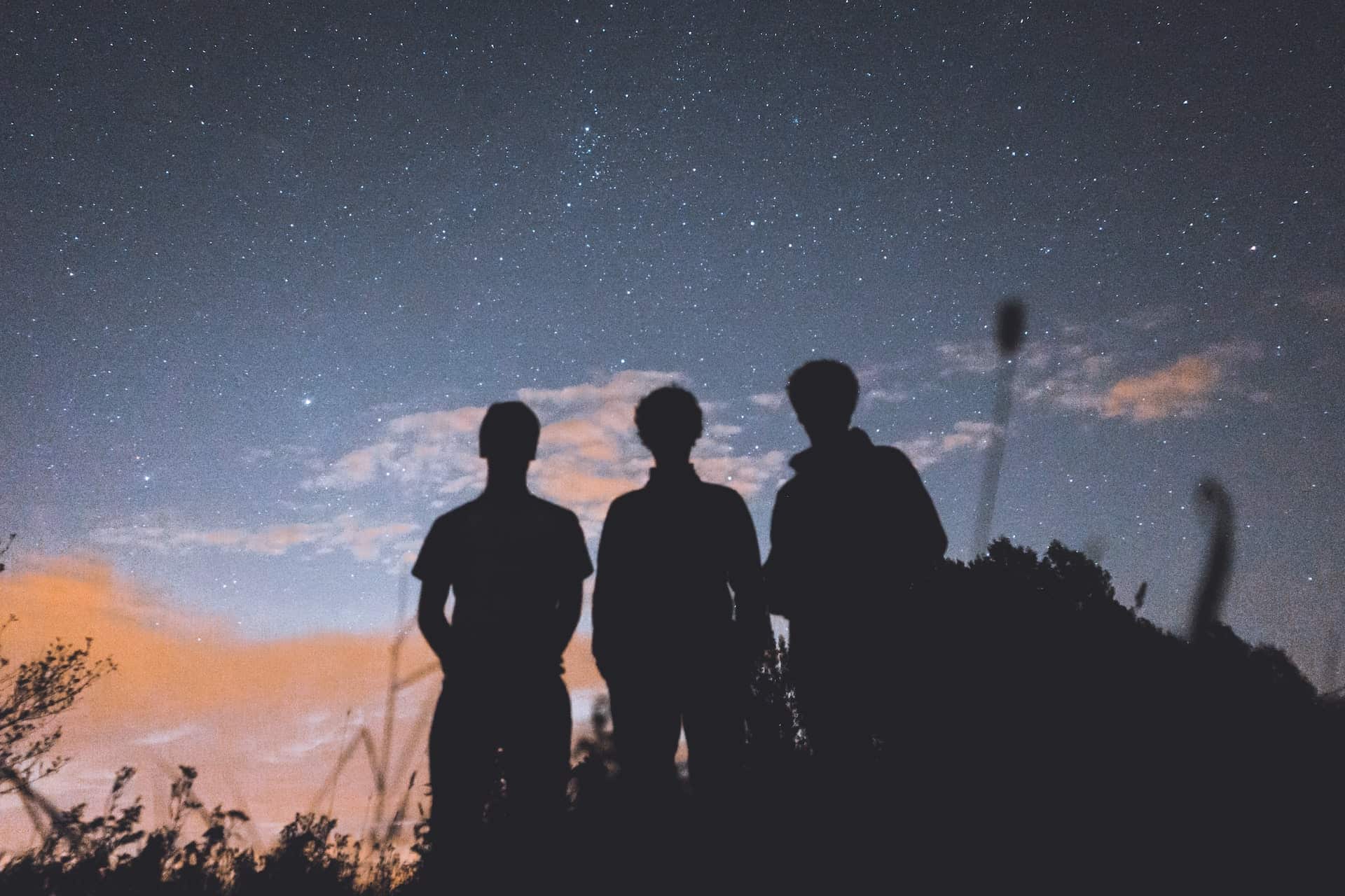 Silhouettes of three men standing under a starry sky.