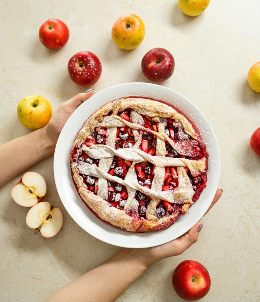 Mixed berry pie on plate surrounded by apples.