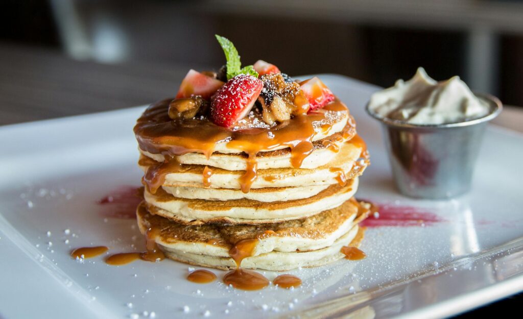 Stack of pancakes with caramel syrup and fruit toppings.